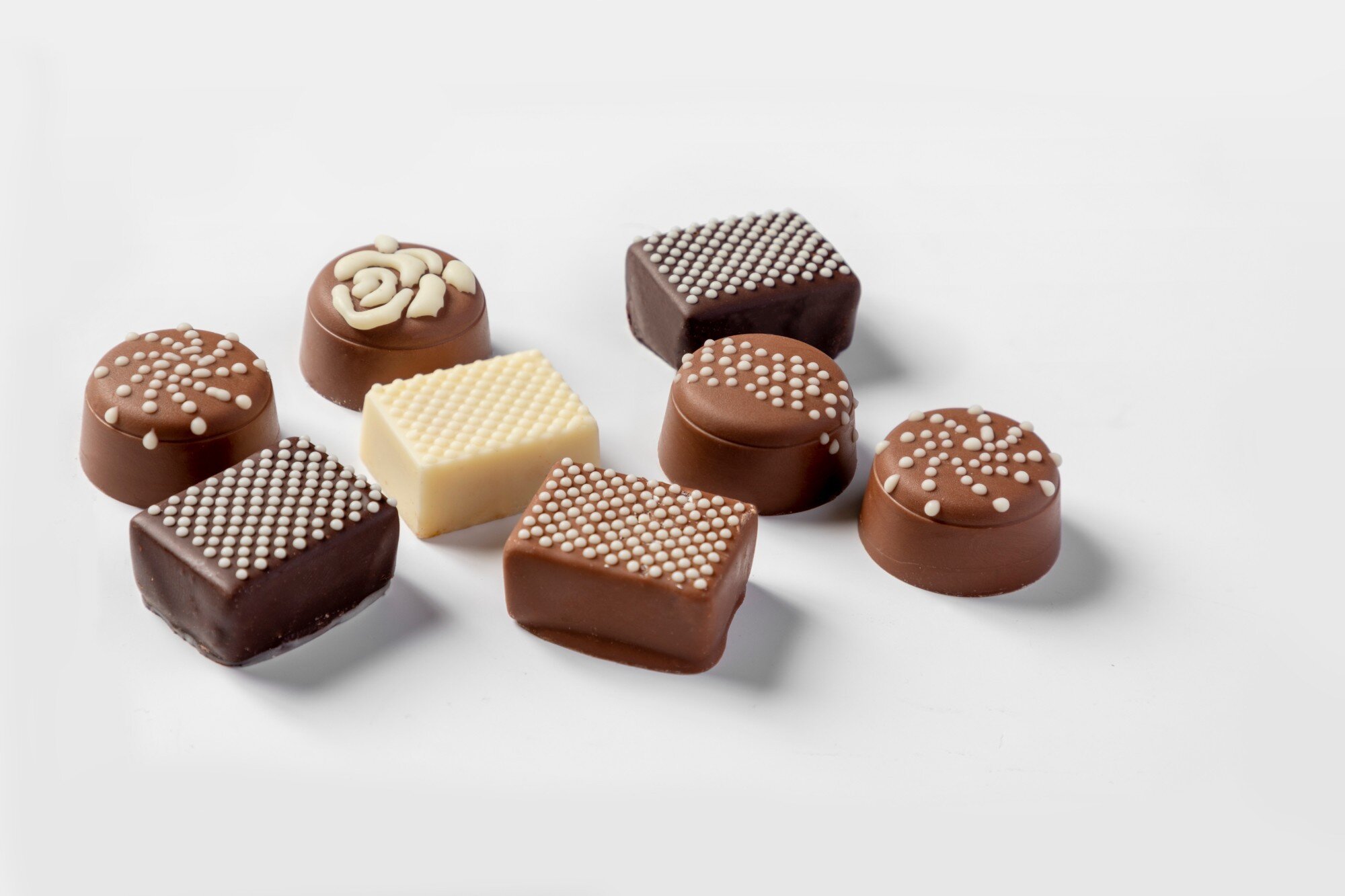 Eight pralines decorated with fine white dots, a dense raster and a rose