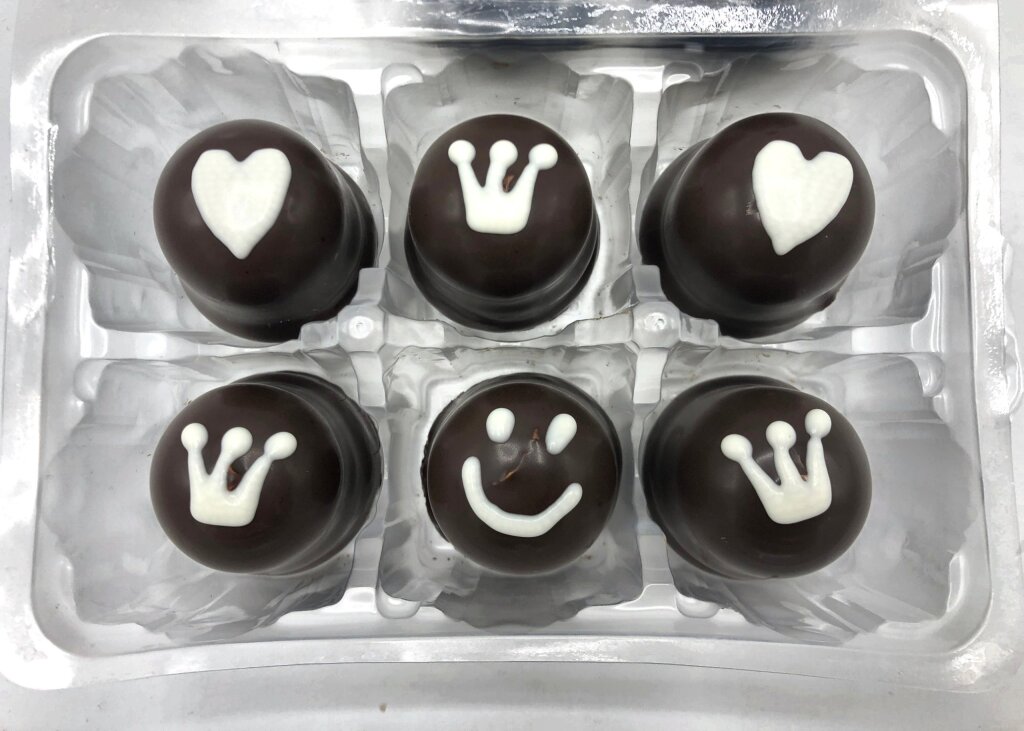 Six chocolate-coated marshmallow treats in a clear blister tray with crowns, hearts and a smiley in white chocolate compound