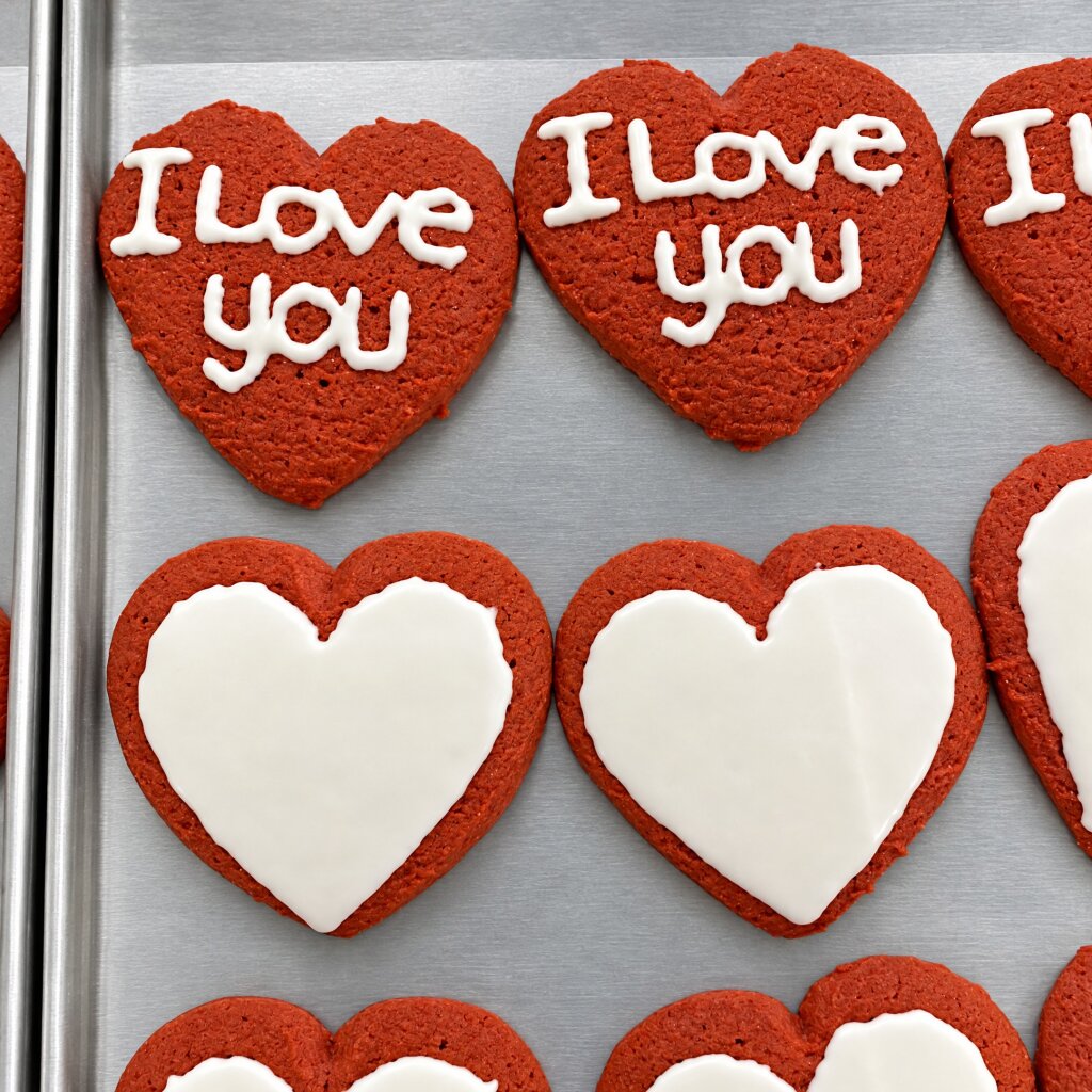 Red heart-shaped cookies with the words I Love you and white hearts on top, on a baking tray