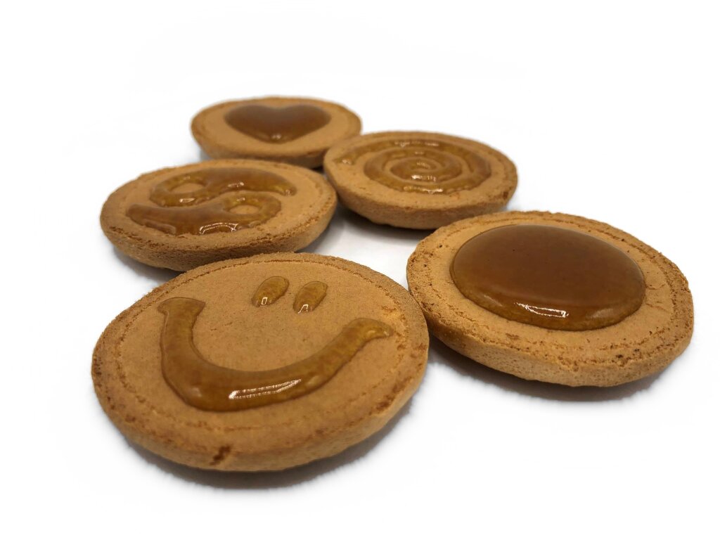 Round biscuits with deposited pectin jam shapes: a heart, a spiral, a swirl, a smiley and a full disc