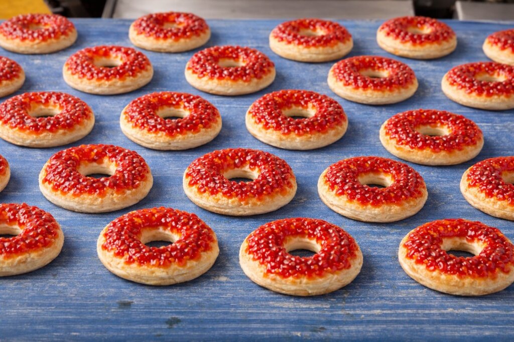 Donut-shaped mini pizzas with tomato sauce deposited in drops, on a blue conveyor