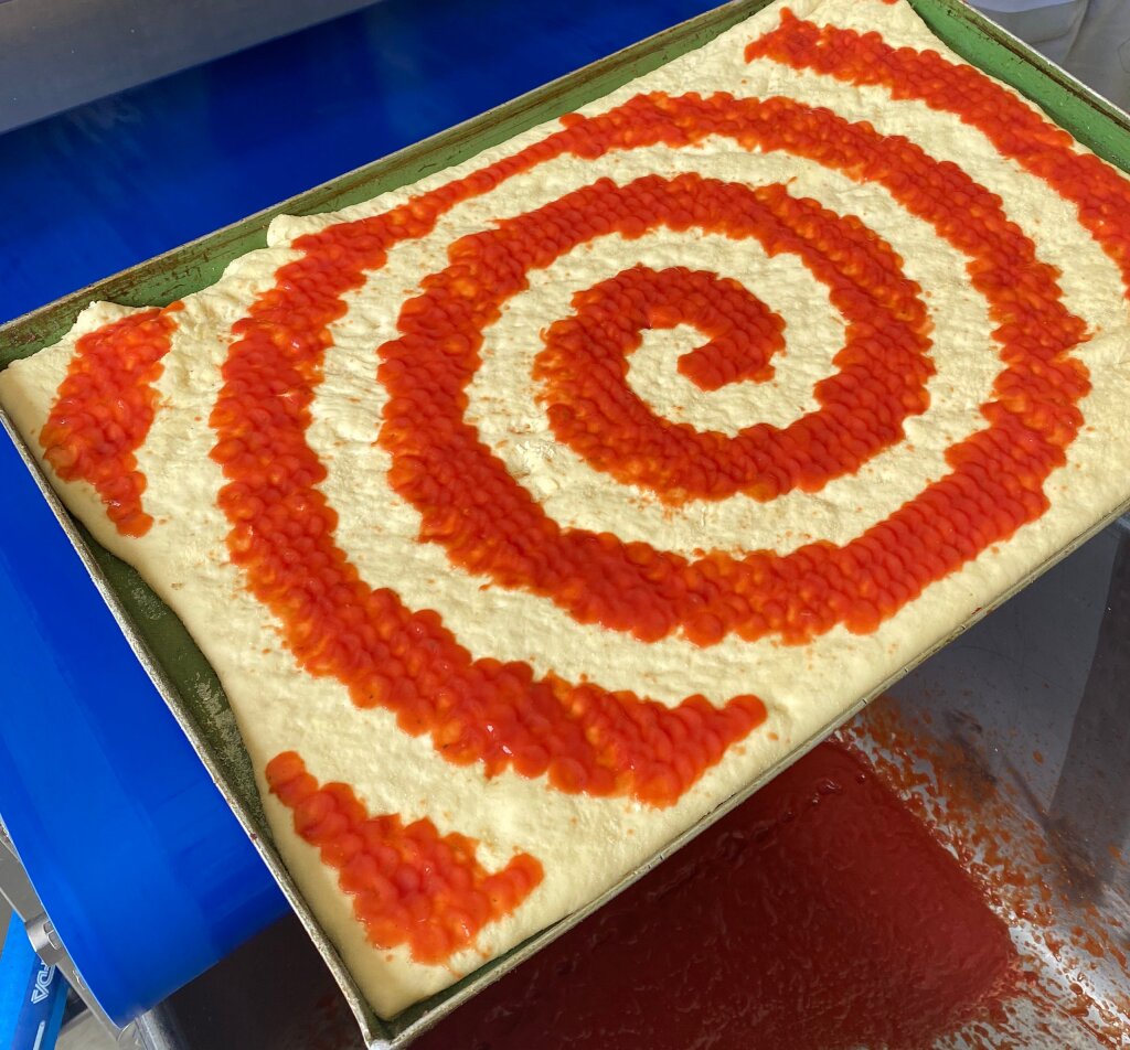 Pizza dough on a baking tray with tomato sauce deposited in a spiral