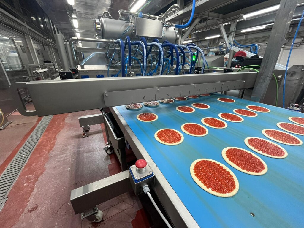 Pizza bases receiving sauce on a production line