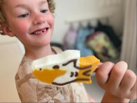 Smiling child holding a shark-shaped ice cream decorated with chocolate lines