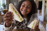 Cheerful girl holding a triangle sandwich with ham, cheese and lettuce from a clear wedge pack