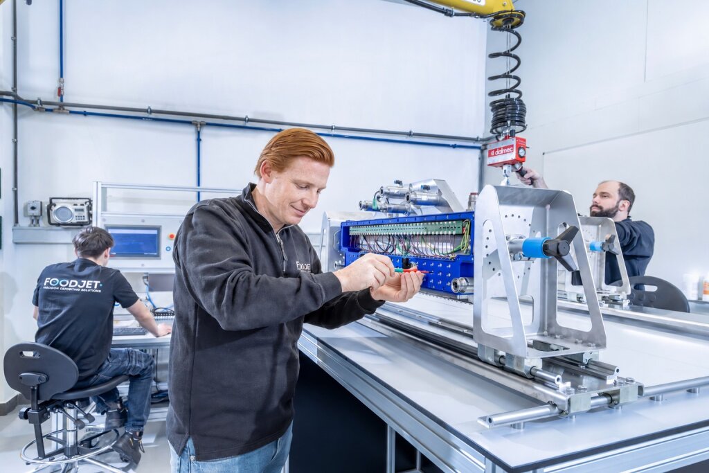 Technician looking at a depositing head while assembling it, with colleagues at work in the background