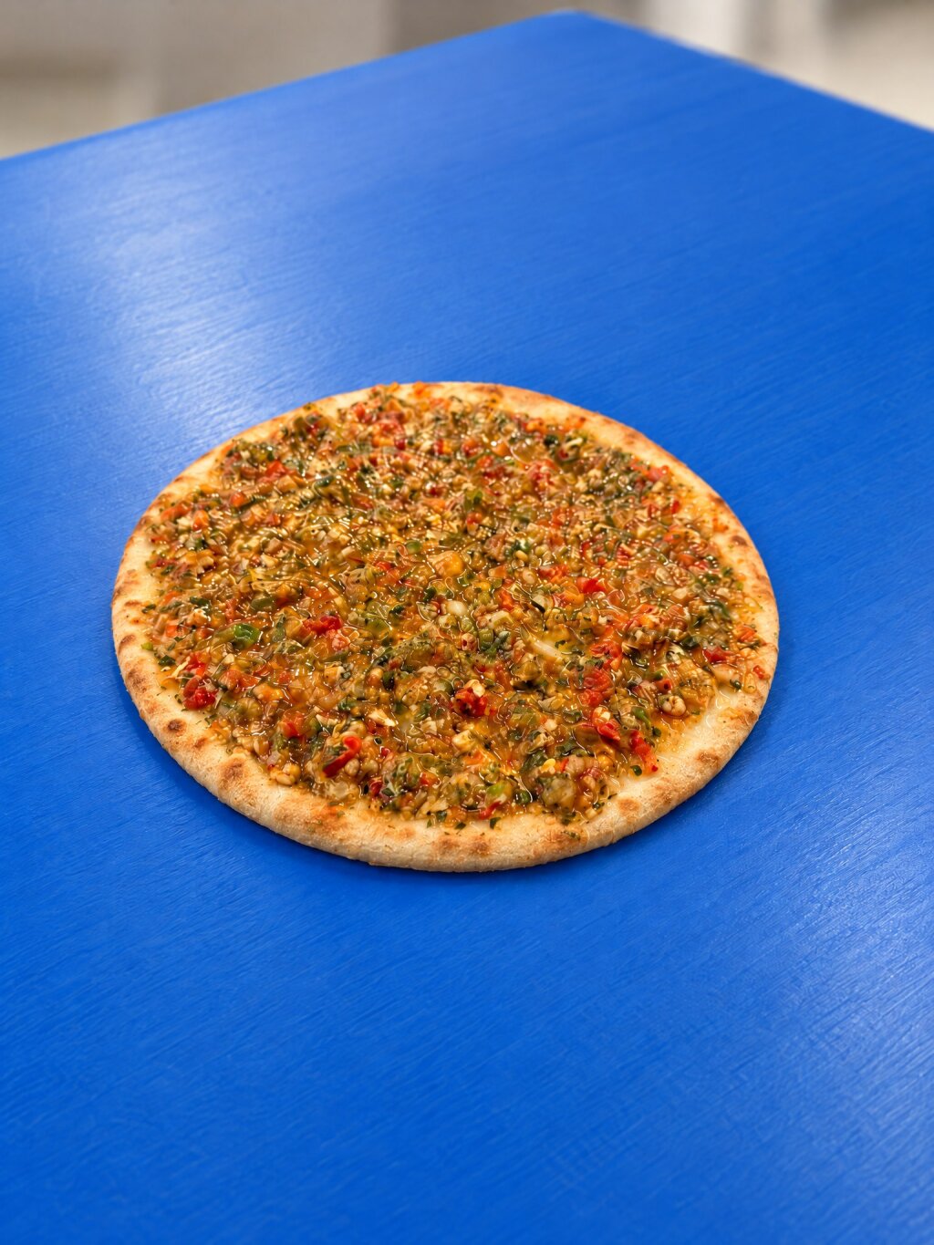Pre-baked pizza base covered with a coarse vegetable and tomato topping, on a blue belt