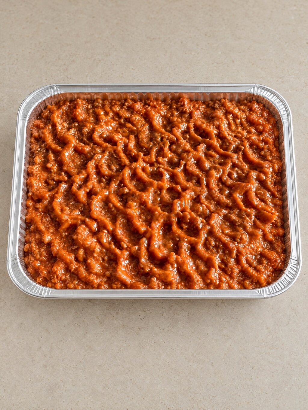 Aluminium tray with an even layer of bolognese sauce in a wavy lattice of ridges