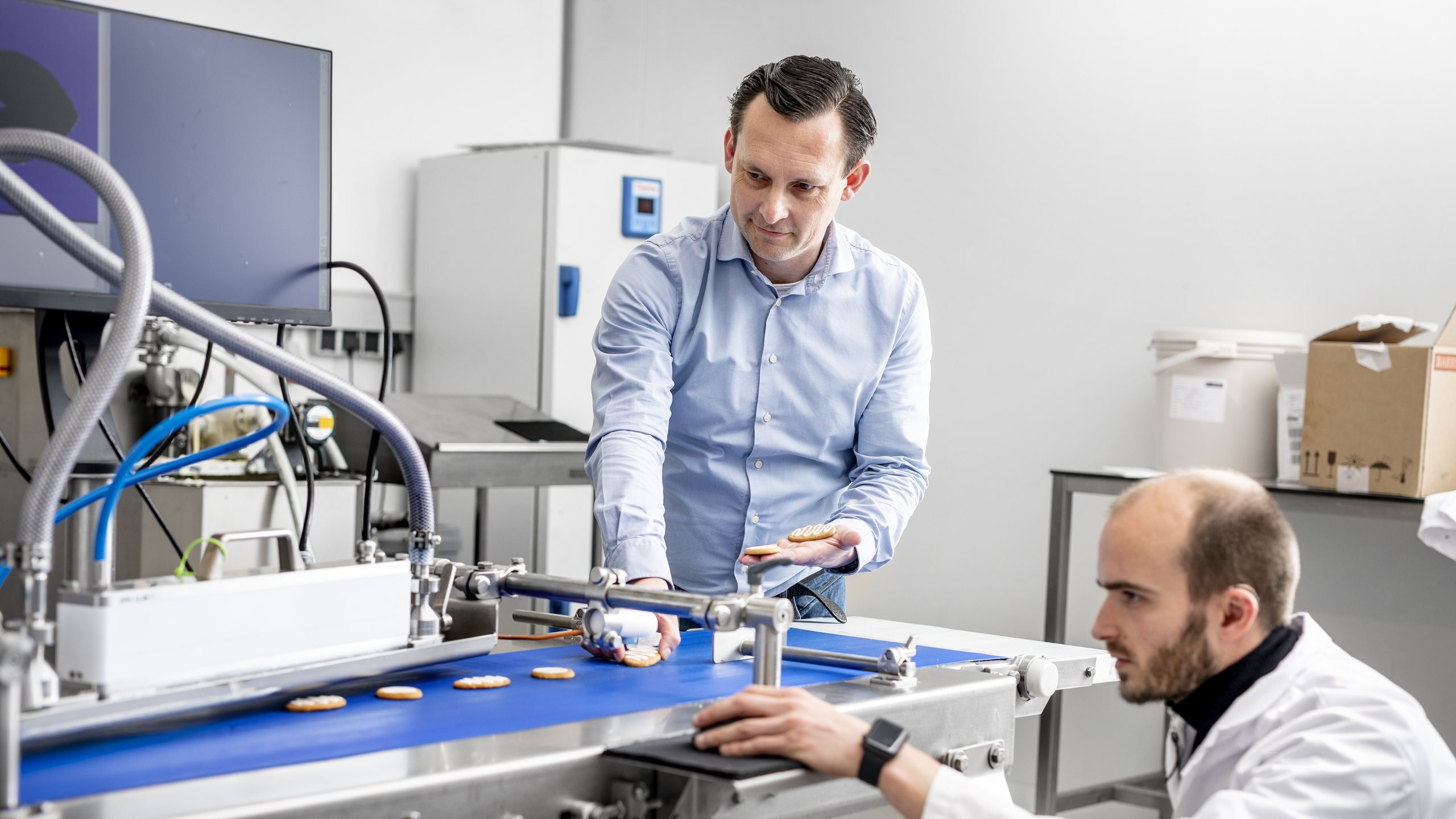 Two people check biscuits on a depositor conveyor during a product trial